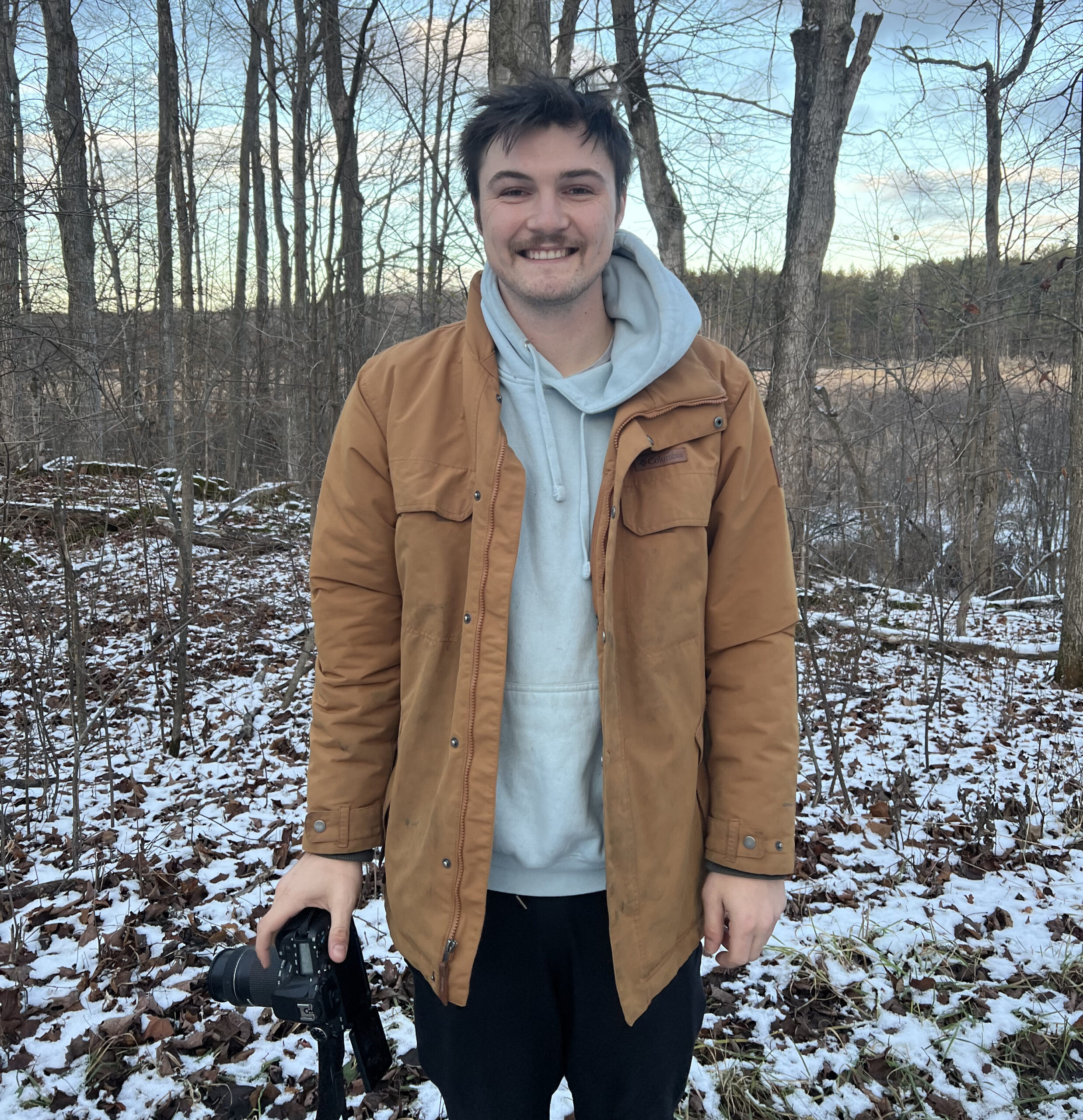 man standing in forest with camera